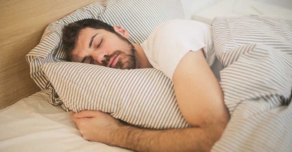 Man sleeping peacefully on striped bedding, embracing relaxation and comfort.